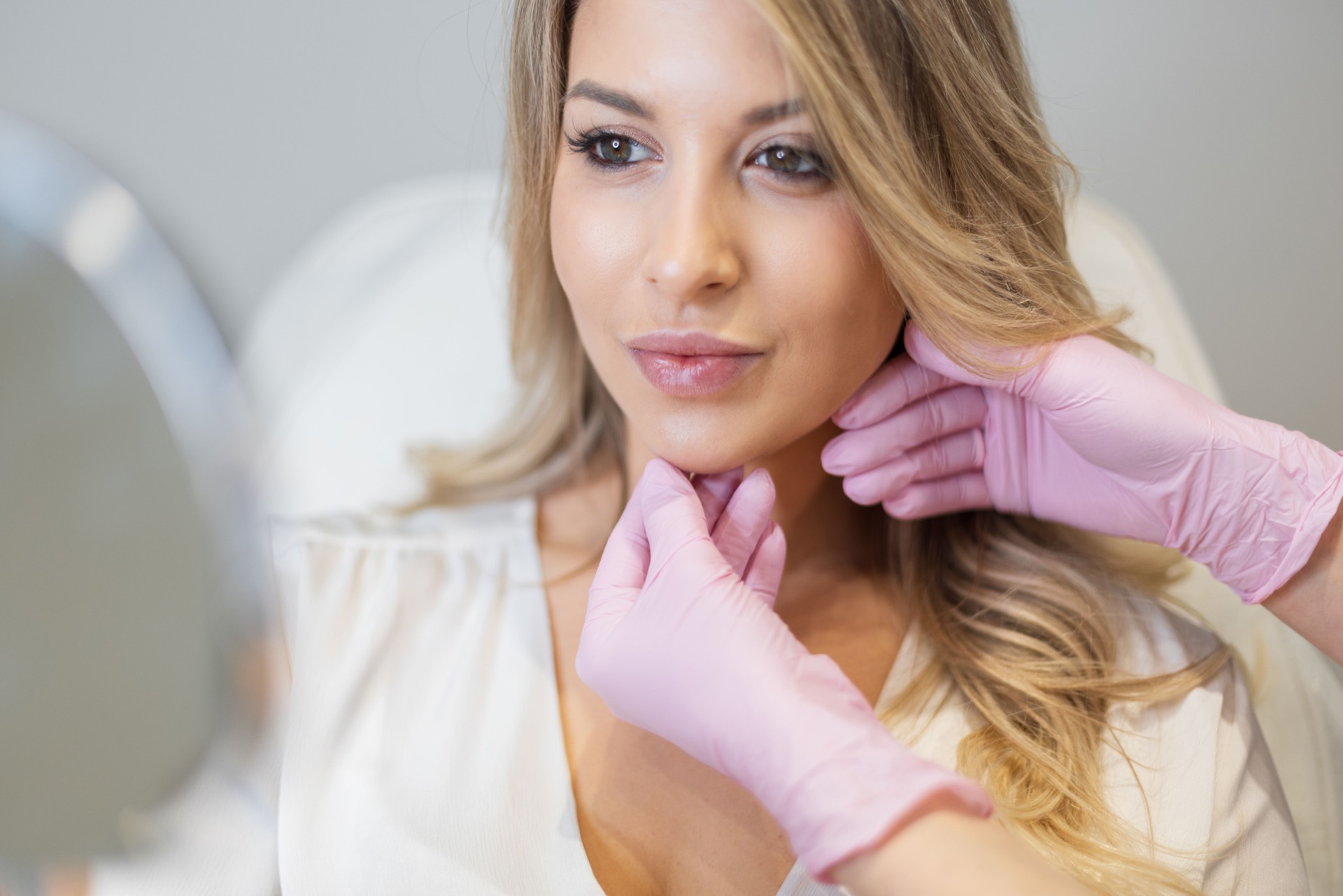 Beautiful fresh woman with clean skin of face and lips in beauty clinic. Professional woman cosmetologist doctor with pink gloves doing procedures